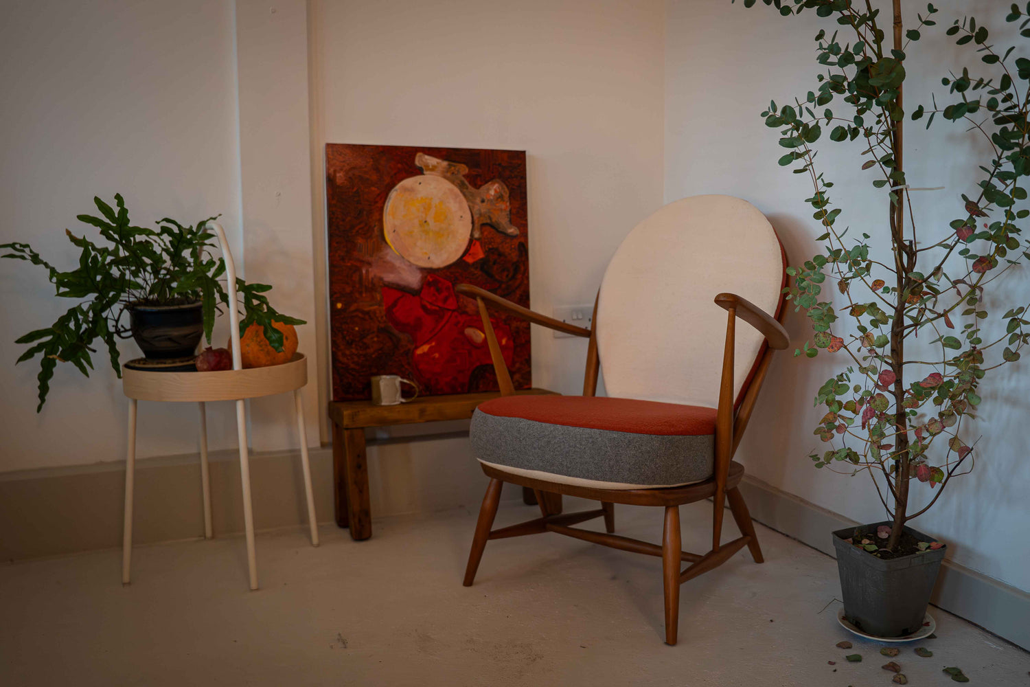 Chair with rust, cream, light grey  cushion in a HOSEF Wandsworth store with plants and a painting on the wall.